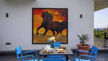 Um pátio com uma mesa posta para o chá, uma pintura de um cavalo e plantas em vasos.
