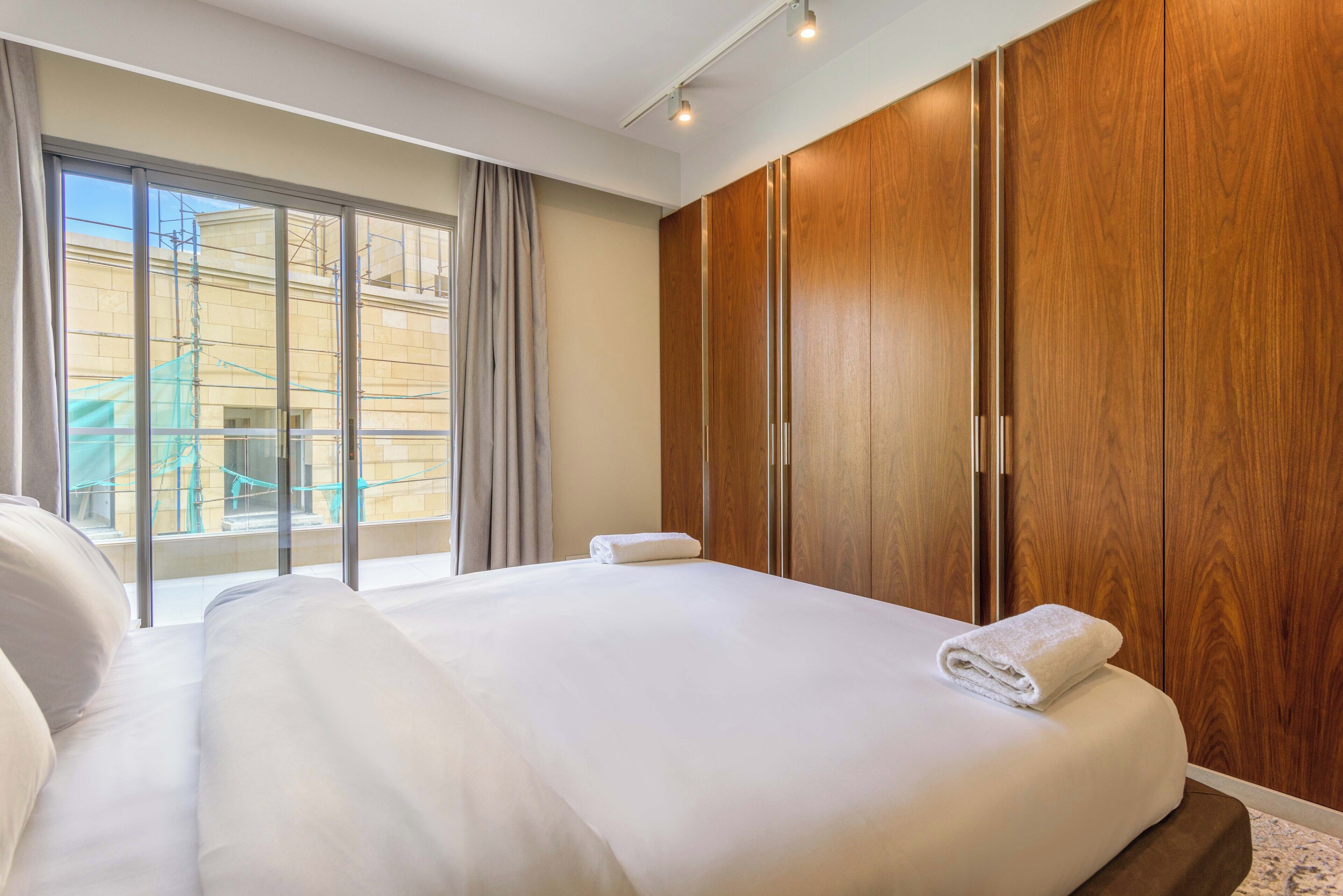 A hotel room with a large bed, wooden wardrobe, and a sliding glass door to the outside.