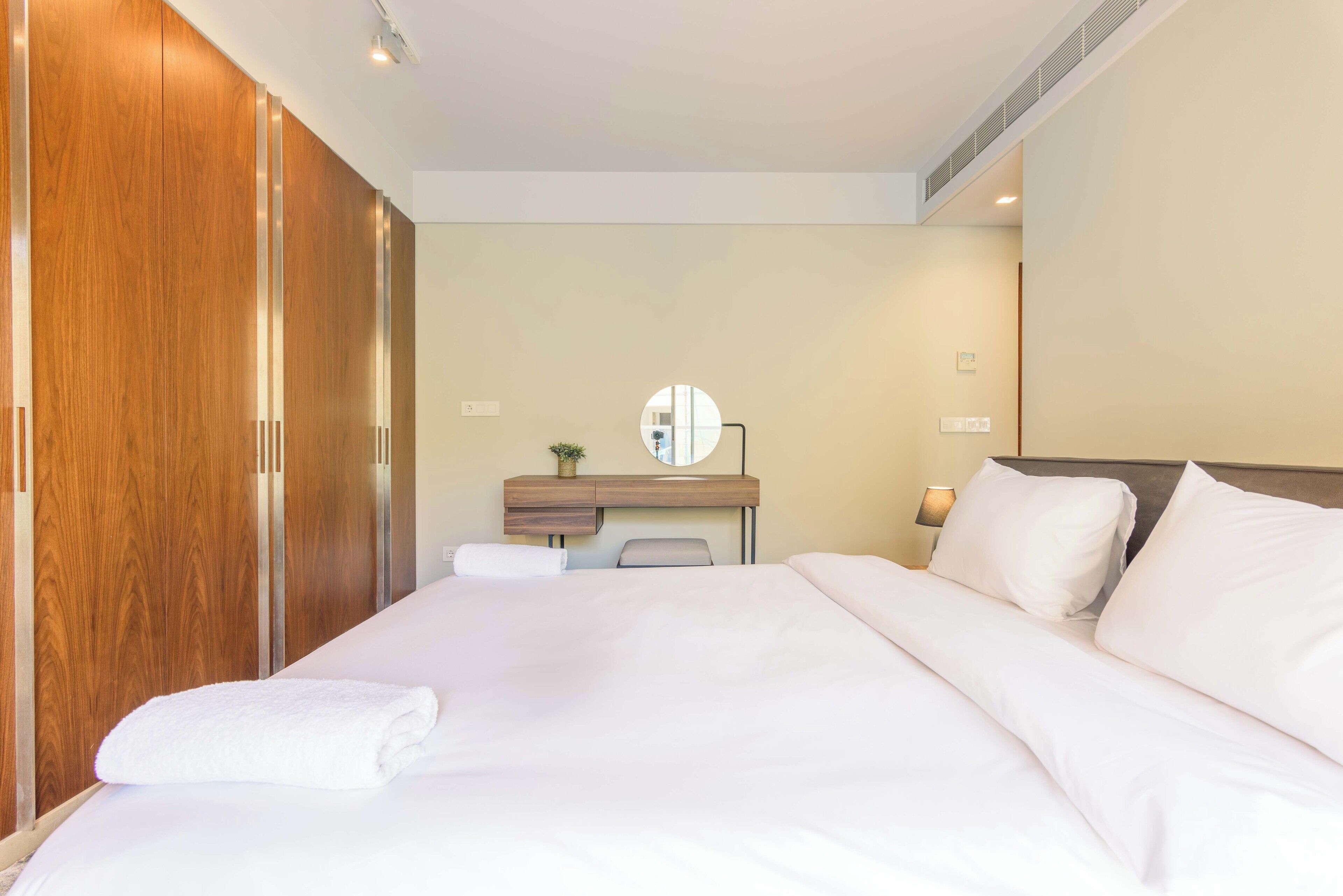 A hotel room with a large bed, a wooden wardrobe, a desk with a mirror, and a small plant.