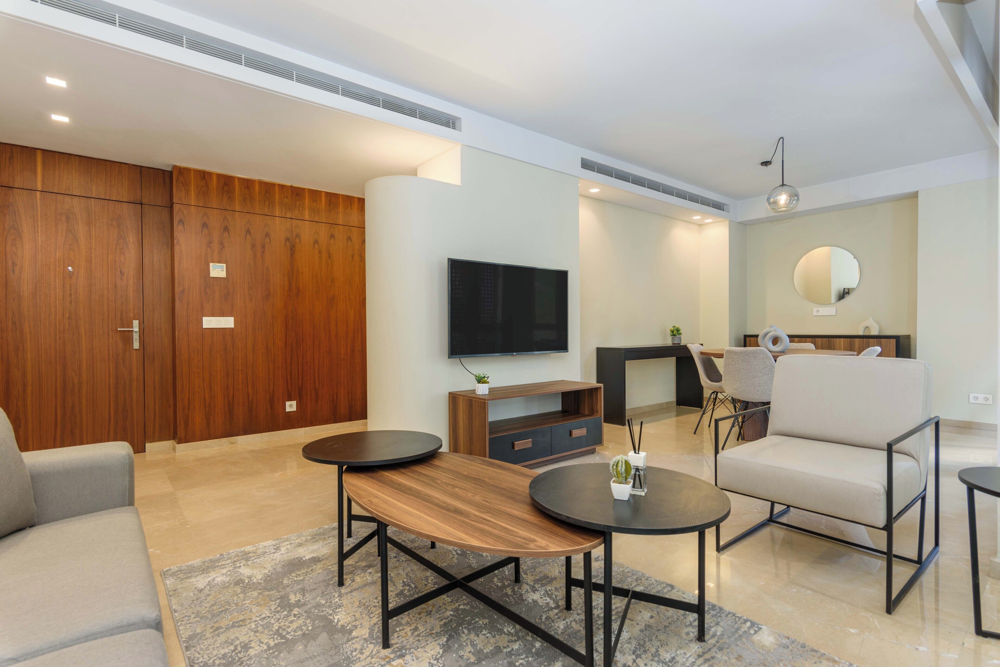 A modern living room with a sofa, two round tables, a TV, and a wooden cabinet.