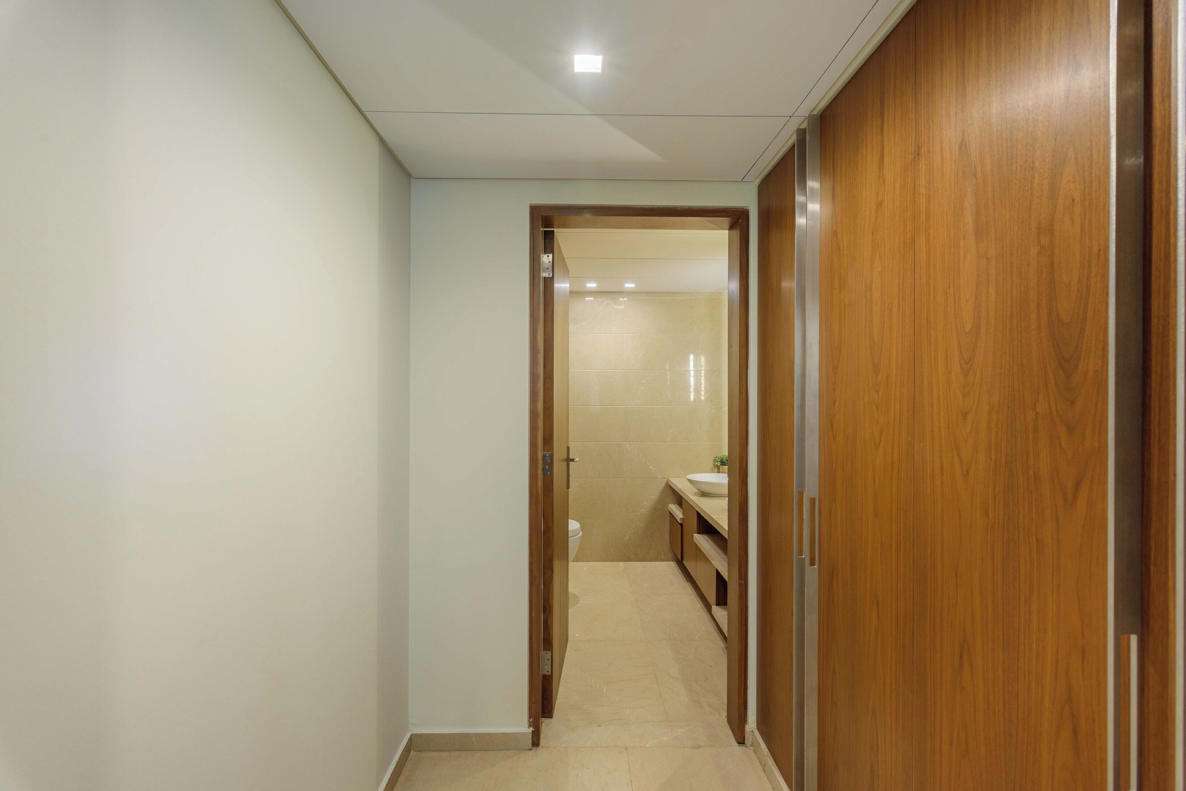 Un pasillo estrecho que conduce a un baño con inodoro, lavamanos y armario de madera.