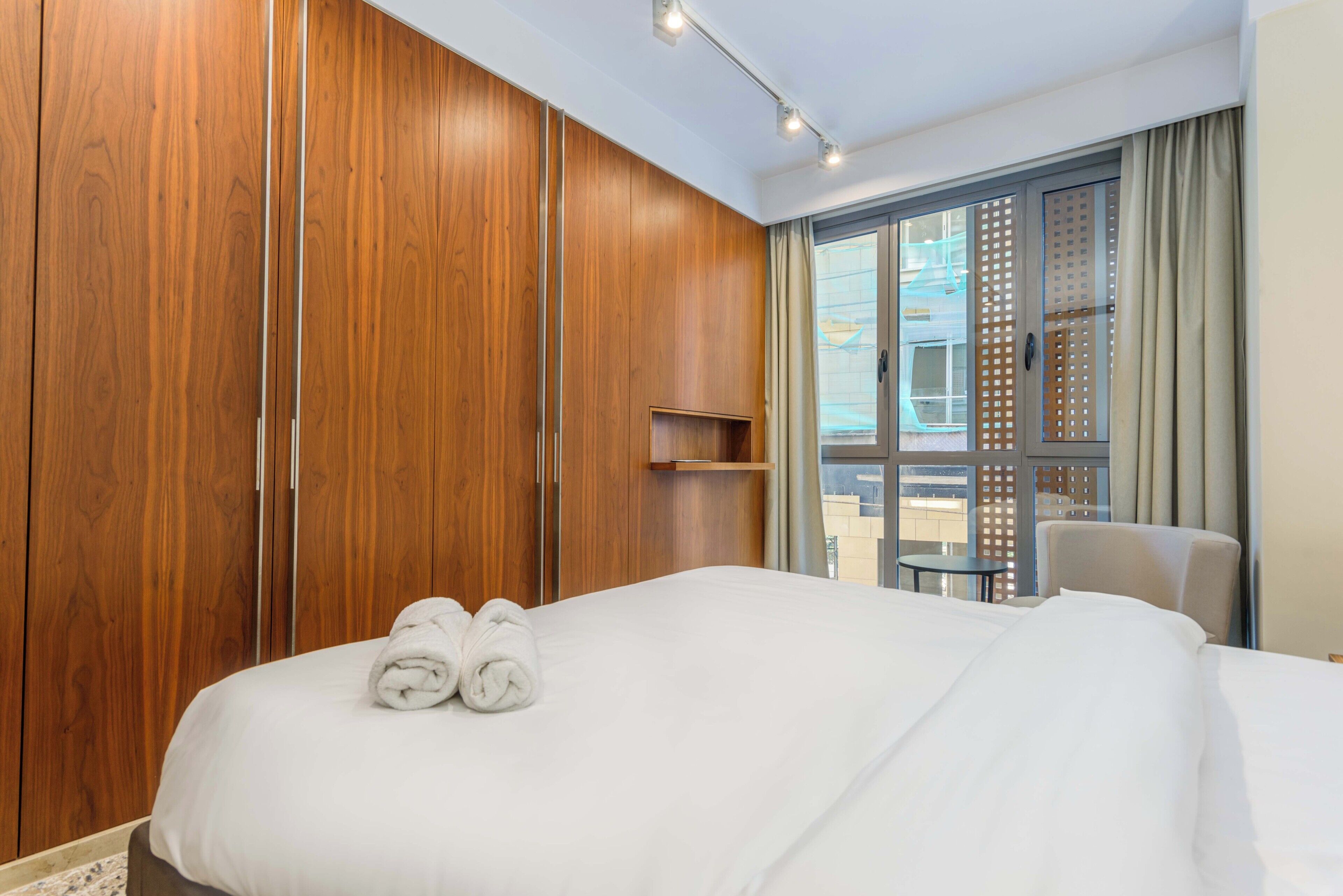 Une chambre d’hôtel avec un grand lit, une armoire en bois et un balcon équipé d’une table et de chaises.