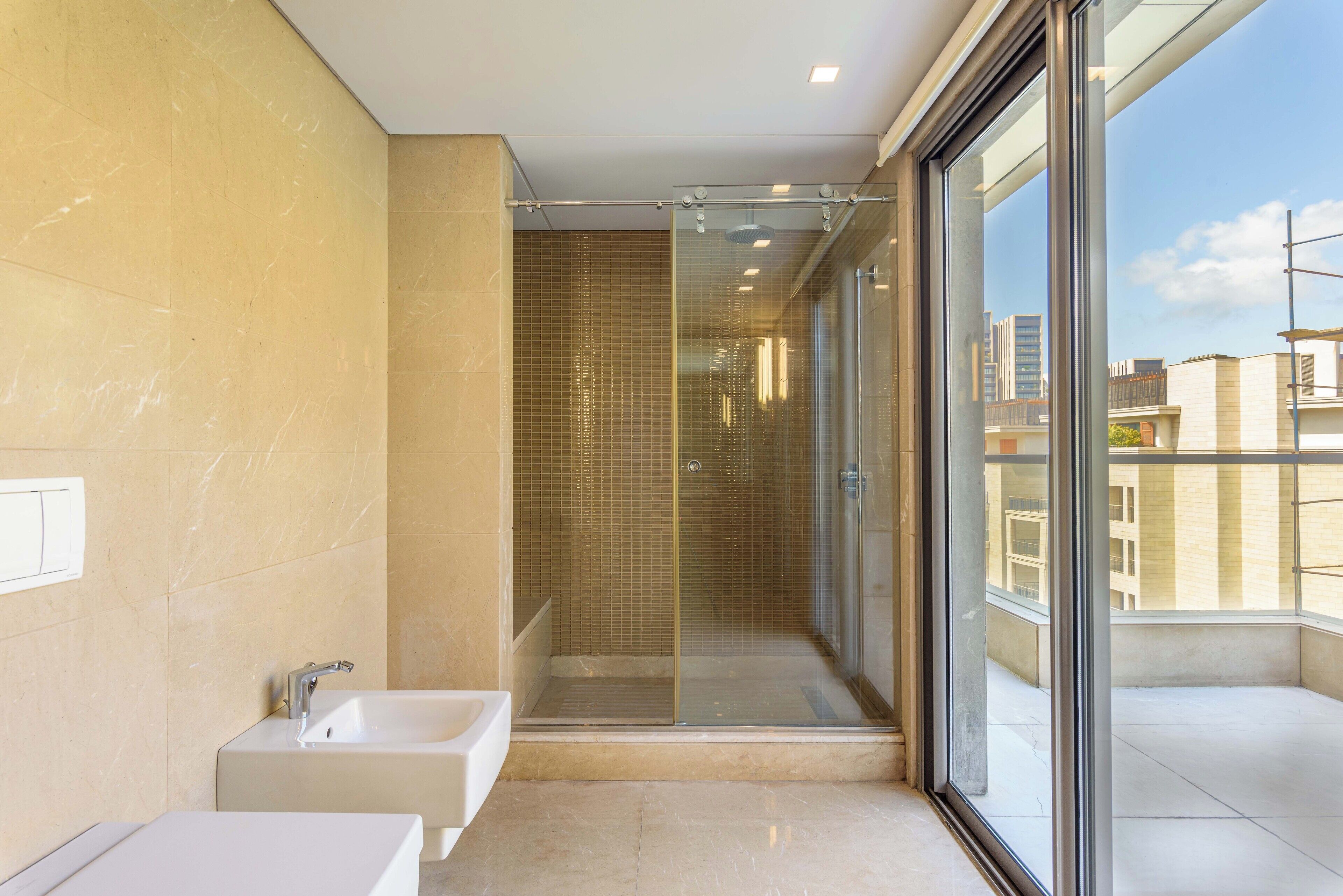 A modern bathroom with a glass-enclosed shower, a standalone bathtub, and a large window offering a city view.