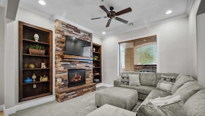 A living room with a stone fireplace, a flat-screen TV, and a ceiling fan. - Pool & Sunshine Retreat - Resort-style Amenities (Hurricane)