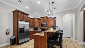 A modern kitchen with wooden cabinets, stainless steel appliances, a granite countertop, and a bar stool. - Pool & Sunshine Retreat - Resort-style Amenities (Hurricane)
