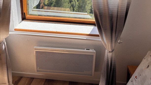 A bedroom with a large window, a radiator, and curtains.