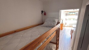 A bunk bed in a room with white walls and a wooden floor. There is a small window with curtains, and a red light fixture on the wall.