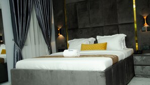 A modern hotel room with a large bed, a bedside table with a phone, and a wall-mounted light fixture. - Kdovehotels&suites (Lagos)