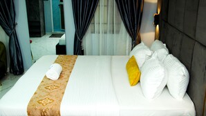 A hotel room with a neatly made bed, a bathroom visible through an open door, and a large window with curtains. - Kdovehotels&suites (Lagos)