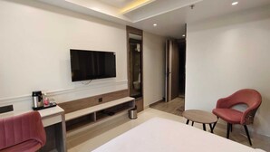 A hotel room with a flat-screen TV mounted on the wall, a bed, a desk with a chair, and a small table with a chair. - Park View (Varanasi)