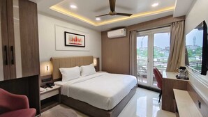 A modern hotel room with a large bed, a desk, a chair, and a view of the city through the window. - Park View (Varanasi)