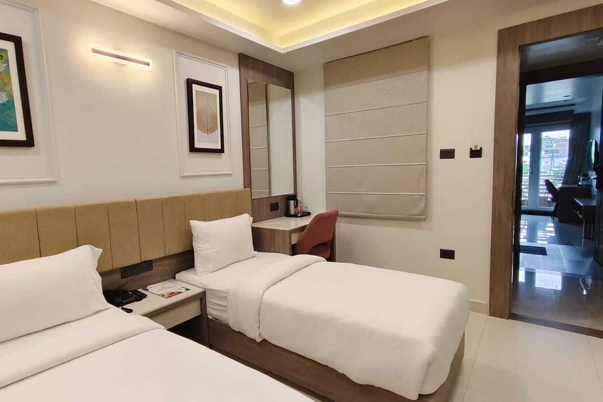A hotel room with two beds, a desk, a chair, a mirror, and artwork on the walls.