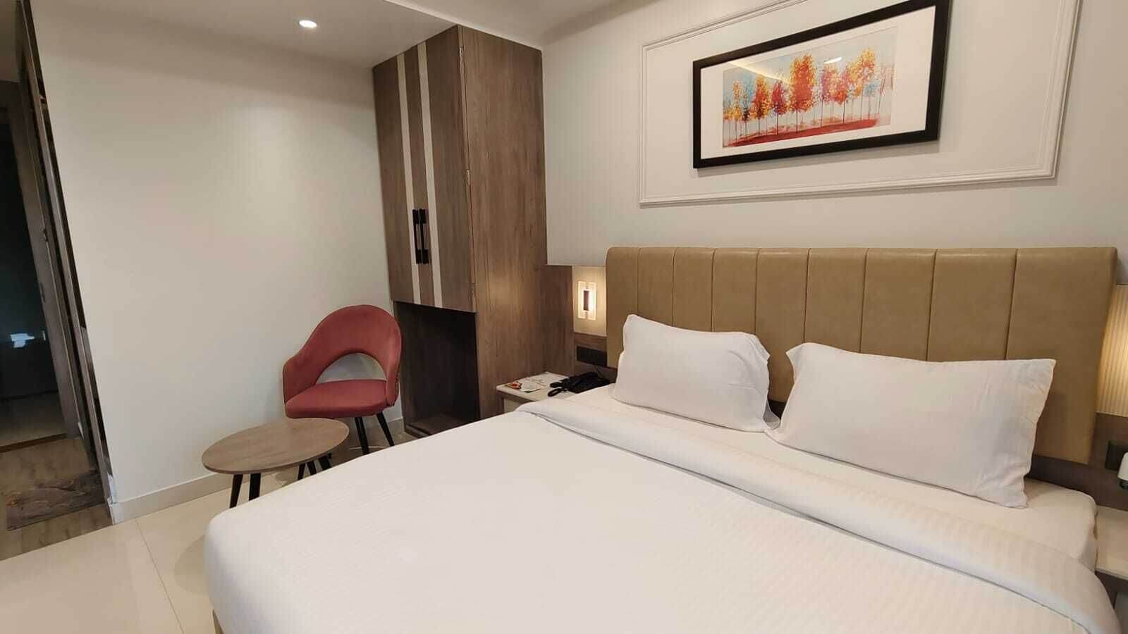 A hotel room with a large bed, a red chair, a small table, and a framed picture on the wall.