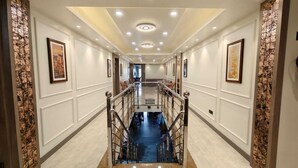 A hotel hallway with a central staircase, white walls, and framed artwork. - Park View (Varanasi)