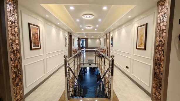 A hotel hallway with a central staircase, white walls, and framed artwork. - Park View (Varanasi)