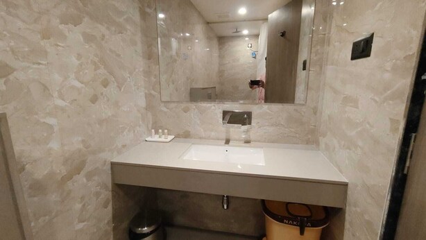 A bathroom with a marble wall, a white sink, and a mirror. - Park View (Varanasi)