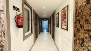 A hallway with a fire extinguisher mounted on the wall, framed artwork on the walls, and a tiled floor. - Park View (Varanasi)