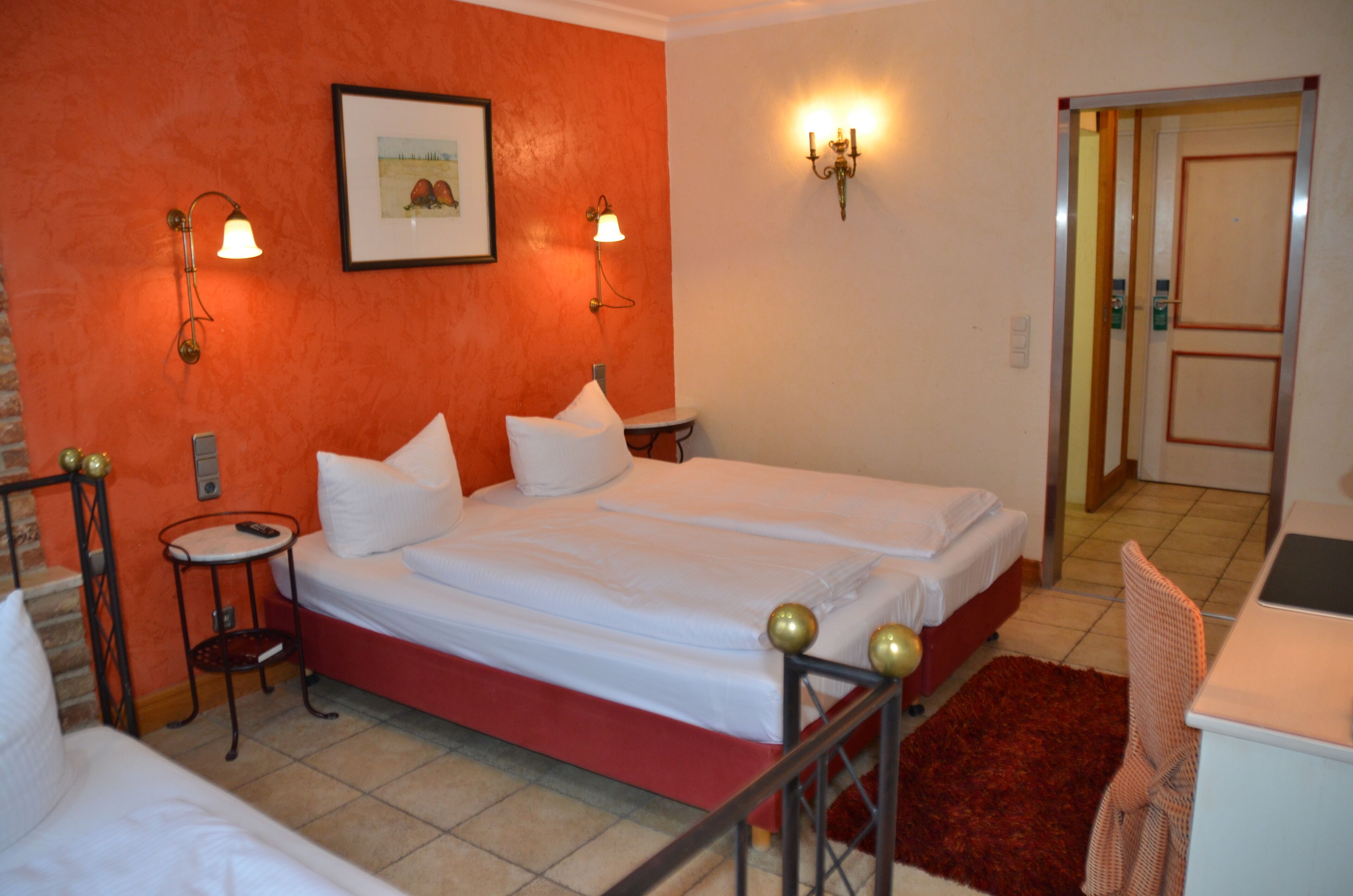Habitación de hotel con una cama doble, dos mesitas de noche, una pared de acento roja y un cuadro enmarcado en la pared.