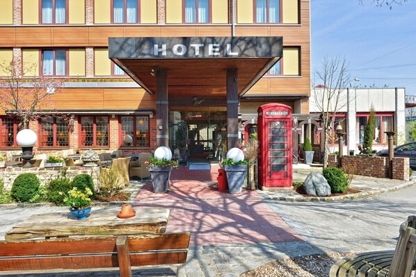 A hotel with a prominent "HOTEL" sign, a red telephone booth, and a well-maintained outdoor area with potted plants and seating.