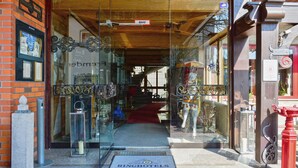 Entrada de un hotel con alfombra roja, un letrero que dice 'RINGHOTELS' y una puerta de vidrio con ornamentación de hierro forjado.