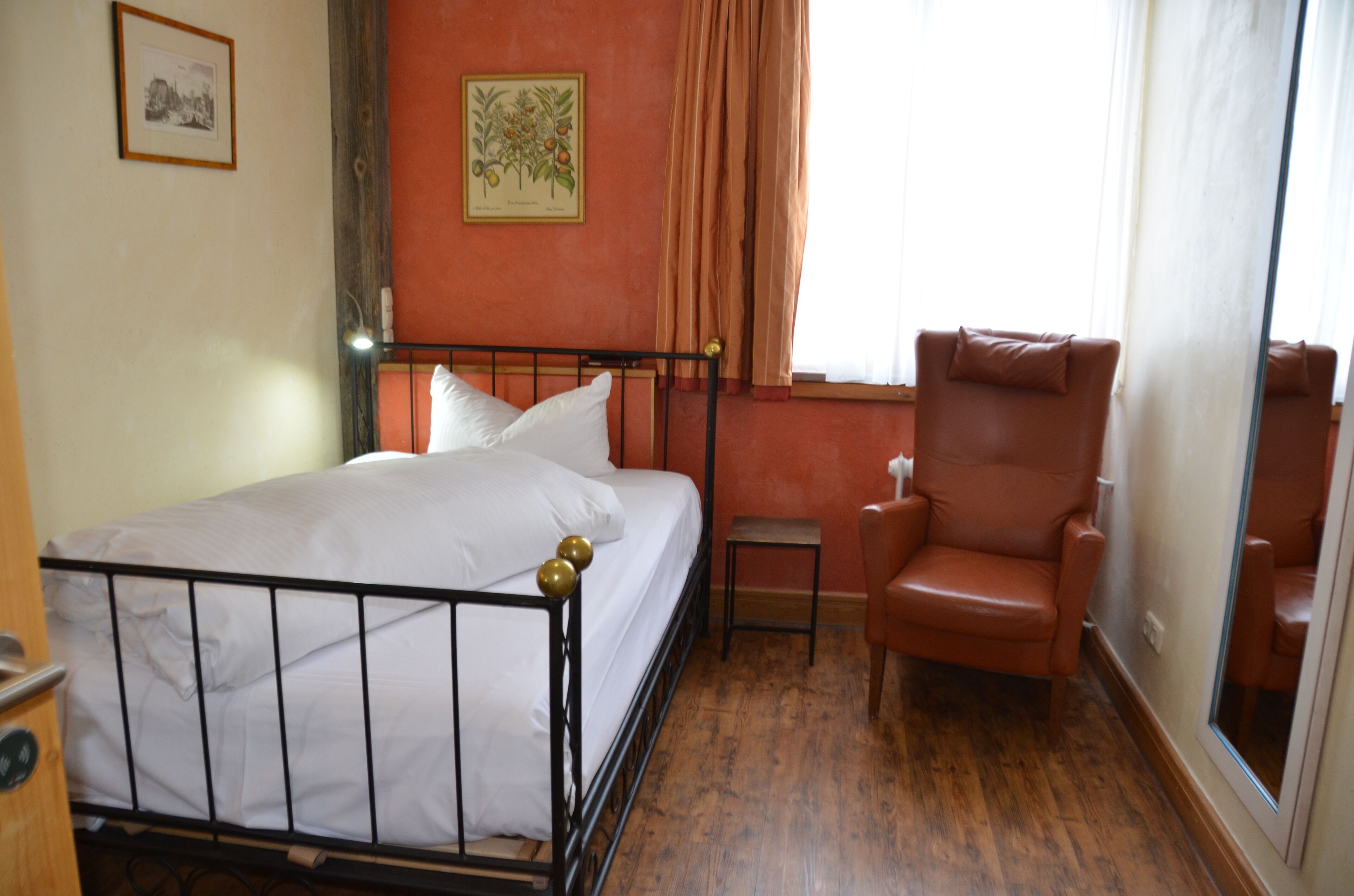 Un dormitorio con cama, una silla, una mesita y una ventana con cortinas.