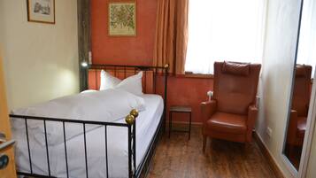 Un dormitorio con cama, una silla, una mesita y una ventana con cortinas.