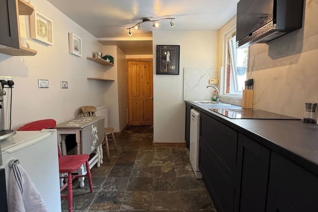 A compact kitchen with a dishwasher, a sink, and a window. There are wooden cabinets and a red chair.