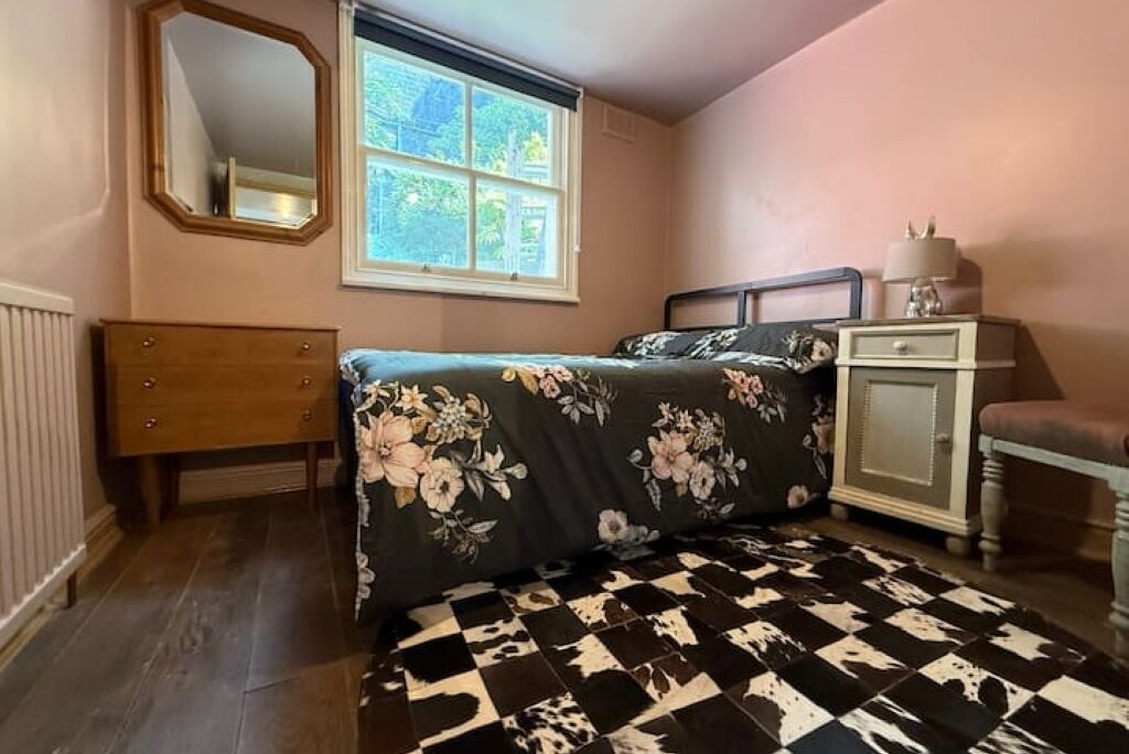 A bedroom with a bed, a dresser, a nightstand, a mirror, and a window.
