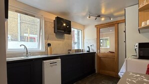 Une cuisine compacte équipée d’un lave-vaisselle, d’un four à micro-ondes et d’une porte en bois donnant sur une autre pièce.