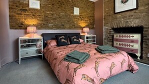 Une chambre avec un mur en briques, un lit recouvert d’une couette à motifs de tigre, deux tables de chevet avec des lampes et une commode avec des tiroirs.