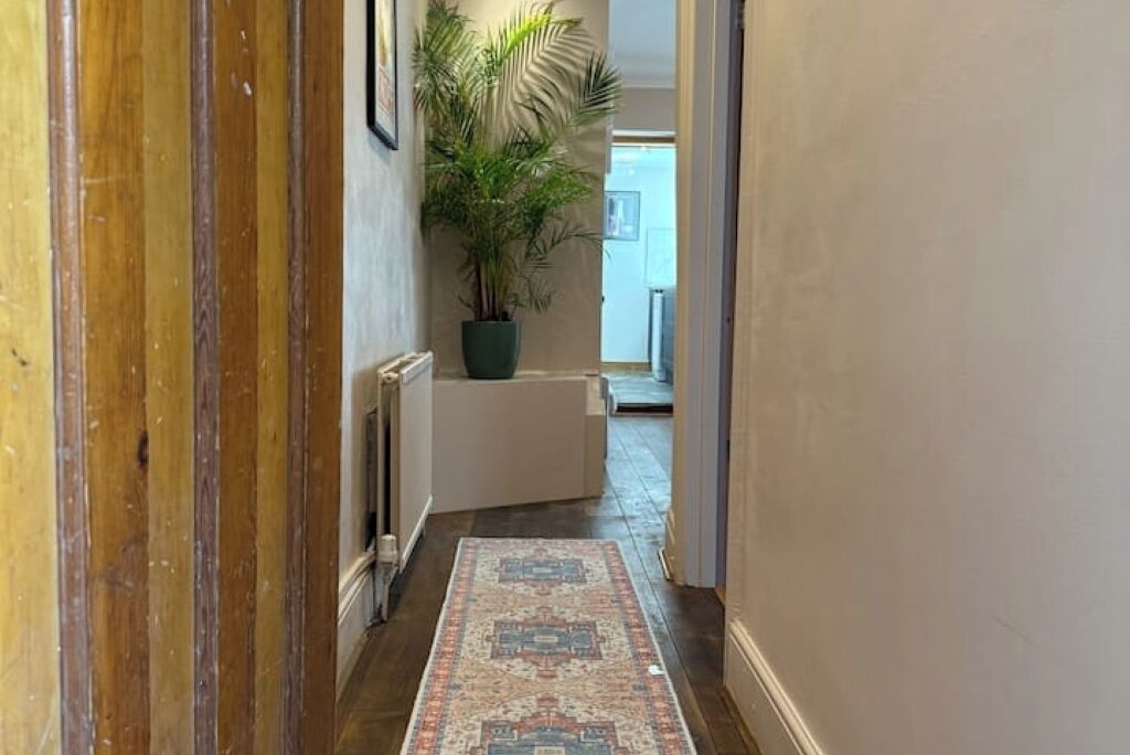 A hallway with a patterned rug, a potted plant, and a white bench.