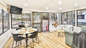 Een moderne eetruimte met een ronde tafel, stoelen en een aan de muur bevestigde televisie.
