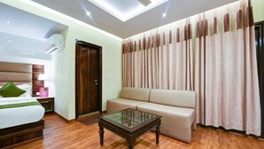 A hotel room with a bed, a sofa, a glass-top coffee table, and a ceiling fan. - Hotel Geet Deluxe (New Delhi)