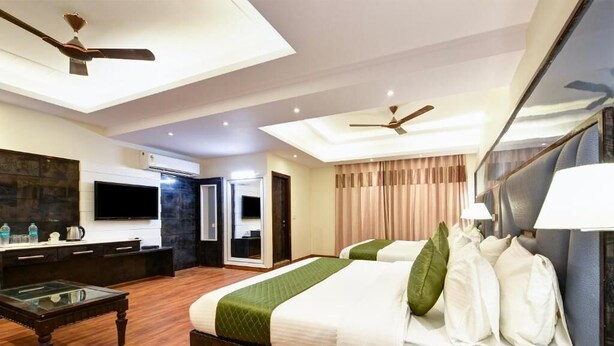 A modern hotel room with a large bed, a glass coffee table, a desk, a flat-screen TV, and a ceiling fan. - Hotel Geet Deluxe (New Delhi)