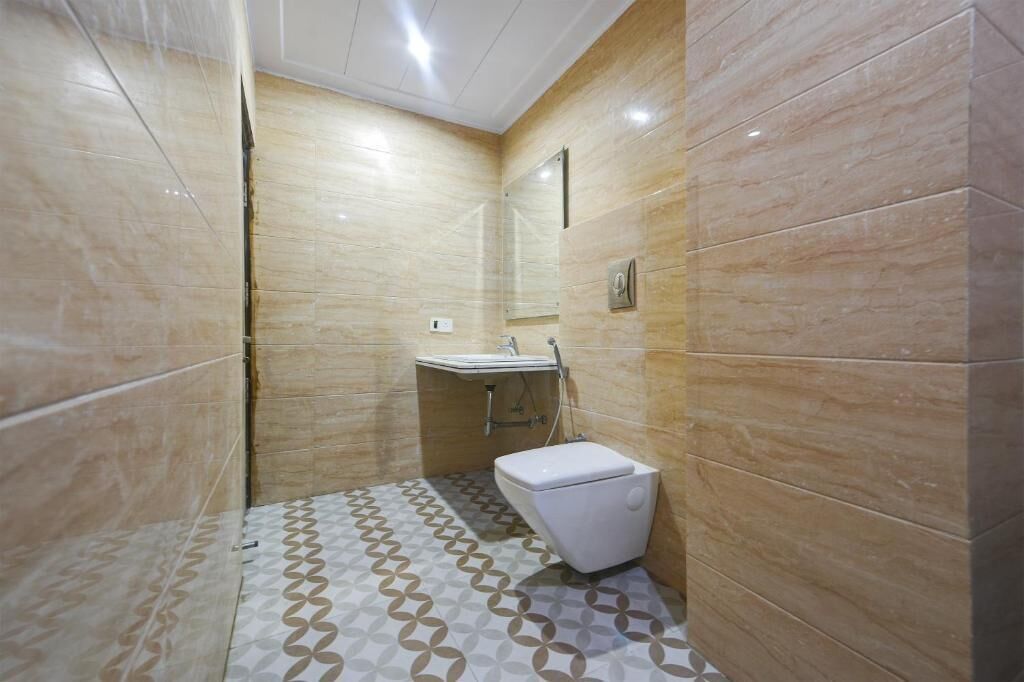 A bathroom with a toilet, sink, and shower area, featuring patterned floor tiles and beige walls.