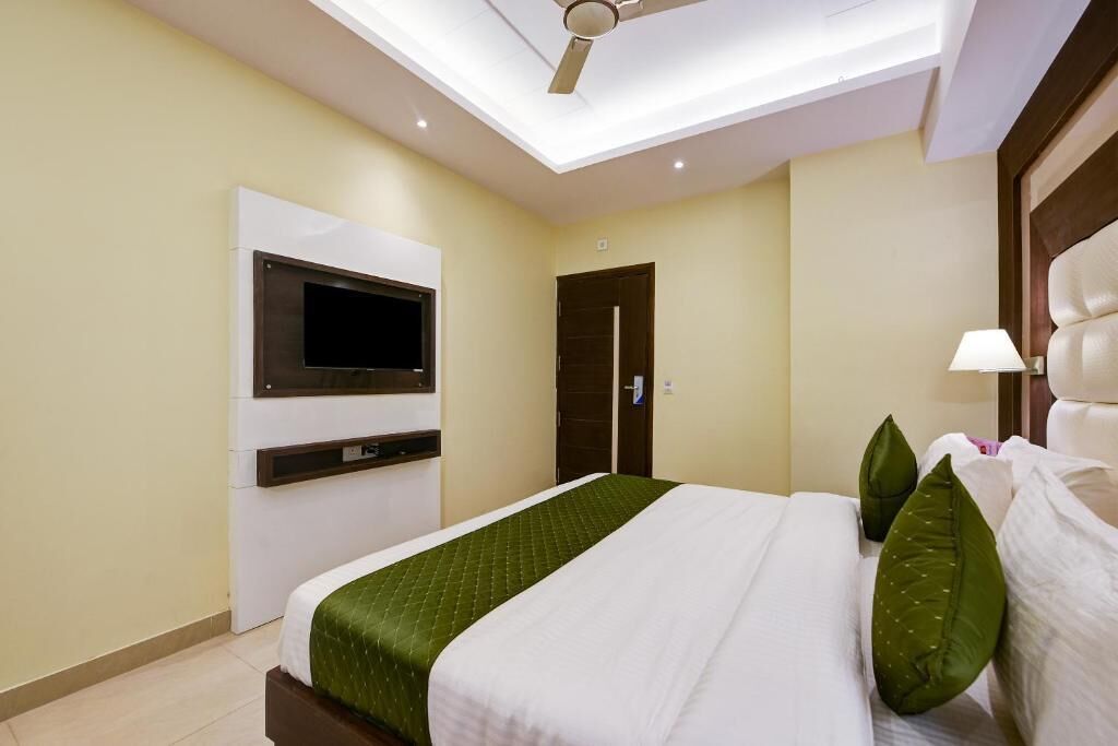 A modern hotel room with a bed, a mounted TV, a ceiling fan, and a door.