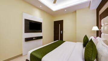 A modern hotel room with a bed, a mounted TV, a ceiling fan, and a door.