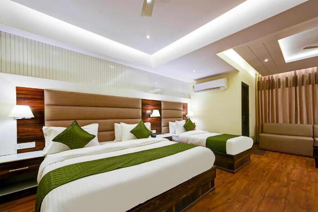 Quarto de hotel com duas camas, um sofá, piso de madeira e design moderno no teto.