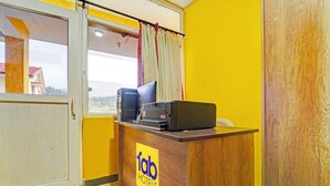 Una recepción con un computador e impresora, una ventana con cortinas y una pared amarilla.