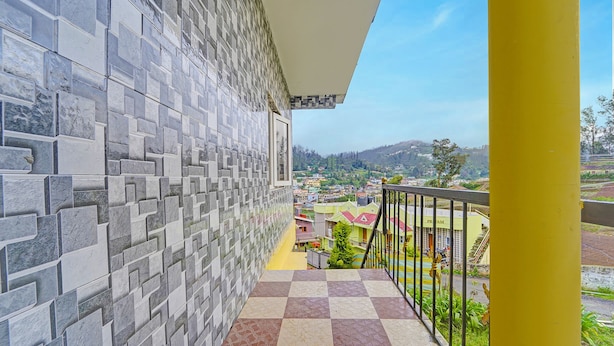Un balcón con piso a cuadros, pared de azulejos y vista a un pueblo con casas y vegetación.