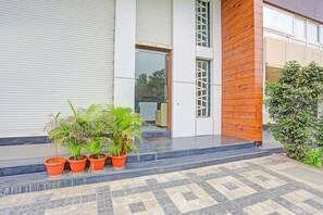 A modern building with a closed shutter, a wooden accent wall, and potted plants on the steps. - Fabhotel Aura Grande (Indore)