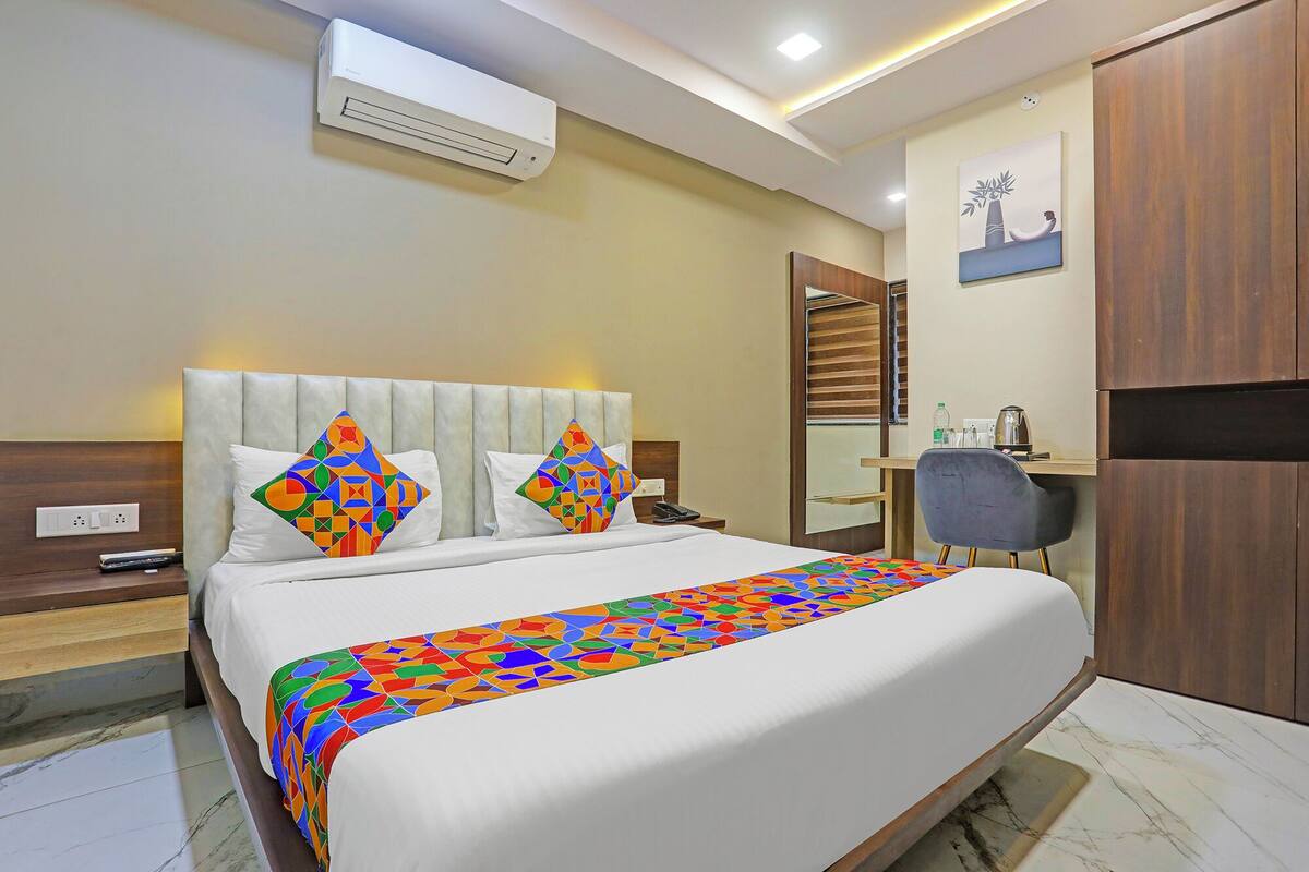 Une chambre d’hôtel avec un grand lit, un bureau, une chaise, un climatiseur et un tableau au mur.