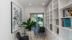 A reading nook with a bookshelf, a framed artwork, and a potted plant.