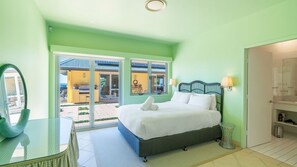 A bedroom with a bed, a glass desk, and a view of an outdoor area.