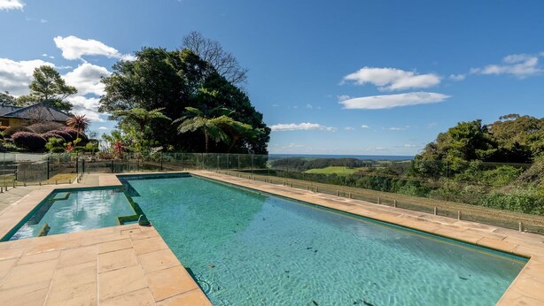 A rectangular swimming pool with clear water, surrounded by a tiled deck and a glass fence. - Flametrees ~ Enchanting holiday rental with absolutely stunning views of the coastline (Jamberoo)