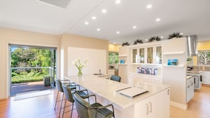A modern kitchen with a central island, bar stools, and a view of greenery outside.