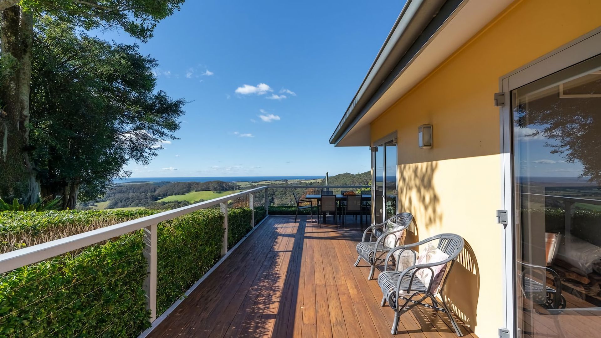 Una terraza de madera con mobiliario exterior, un ventanal y vistas al paisaje.