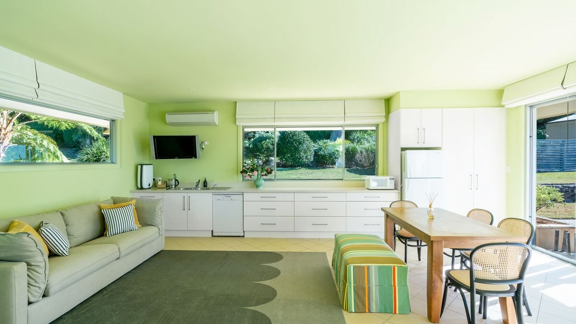 Una cocina moderna con armarios blancos, un comedor con mesa y sillas de madera, y un sofá con cojines a rayas.