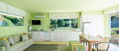 Una cocina moderna con armarios blancos, un comedor con mesa y sillas de madera, y un sofá con cojines a rayas.