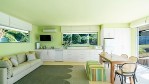 A modern kitchen with white cabinets, a dining area with a wooden table and chairs, and a sofa with striped cushions.